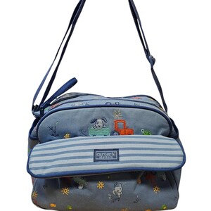 May include: Blue baby bag with a flap featuring horizontal blue and white stripes. The bag has a shoulder strap and is decorated with embroidered images of a dog, a tractor, and other playful designs. The text "carter's starters" is visible.