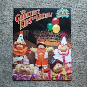 May include: A vintage Cabbage Patch Kids poster featuring five Cabbage Patch Kids dolls dressed as clowns. The dolls are standing in front of a circus tent with a crowd of people in the background. The poster has the text "The Greatest Kids on Earth!" and "Cabbage Patch Kids Circus Time" on it.
