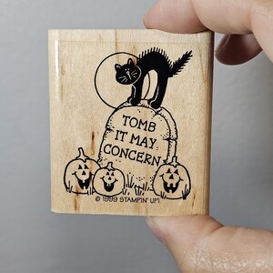 Pode incluir: Um carimbo de madeira com um gato preto em uma l&aacute;pide com a frase "TOMB IT MAY CONCERN" e tr&ecirc;s ab&oacute;boras esculpidas. O carimbo tamb&eacute;m inclui o texto "&copy; 1999 STAMPIN' UP!".