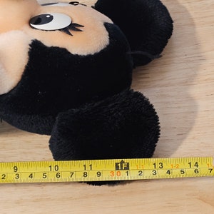 May include: Black and tan plush toy of Mickey Mouse with a measuring tape showing the toy is 11 inches long.