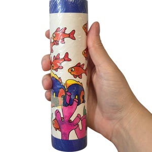 May include: A roll of wallpaper featuring a vibrant underwater scene. The design includes cartoon fish in shades of red, orange, and blue, along with pink coral. The top and bottom edges of the roll are trimmed with a dark blue border.