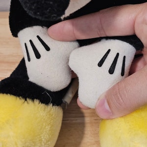 May include: Black and yellow plush toy with white gloves. The toy has a black face and large, round ears.