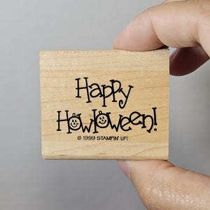 Pode incluir: Um carimbo de madeira com as palavras "Happy Halloween!" em preto, com uma fonte extravagante. A palavra "Halloween" apresenta rostos de jack-o'-lantern em vez das letras "o". O carimbo tamb&eacute;m inclui o texto "&copy; 1999 STAMPIN' UP!"