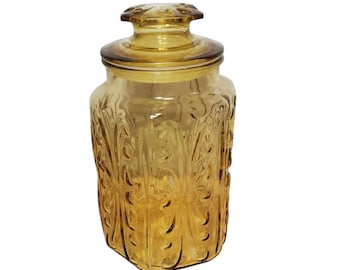 May include: Amber glass jar with a lid and a floral pattern. The jar is square shaped and has a textured surface.