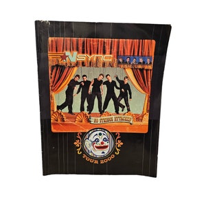 May include: A black and white program booklet for the *NSYNC No Strings Attached Tour 2000. The cover features a cartoon clown with a red nose and a colorful hat. The band members are pictured as puppets on a stage.