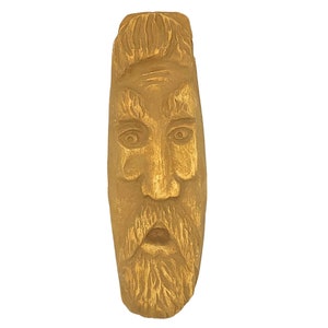 May include: A wooden carving of a face with a long beard and a surprised expression. The carving is painted gold.