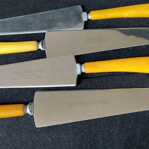 May include: A set of four cake servers with bright yellow handles and polished stainless steel blades. Each server features a flat, wide, triangular-shaped head with a rounded tip and a silver-toned metal bolster connecting the handle to the blade.