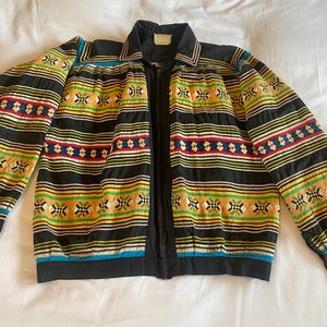 May include: A black jacket with a zip fastening and colourful geometric patterns. The jacket has long sleeves and a collar.