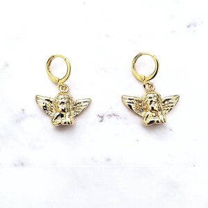 May include: Gold hoop earrings with a small angel charm hanging from each hoop.