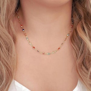 May include: A gold chain necklace with small, colorful beads. The beads are in shades of red, orange, blue, and green.