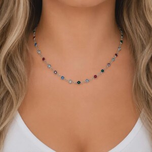 May include: A silver-toned chain necklace featuring evenly spaced, round, multi-colored gemstones in shades of red, blue, green, and clear. The delicate metal links connect each individual stone, creating a continuous, lightweight, and circular design.