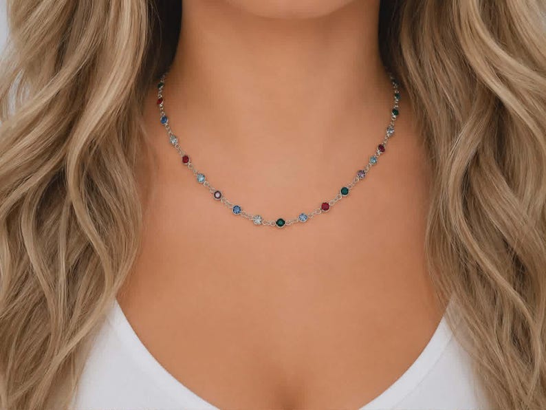 May include: A silver-toned chain necklace featuring evenly spaced, round, multi-colored gemstones in shades of red, blue, green, and clear. The delicate metal links connect each individual stone, creating a continuous, lightweight, and circular design.