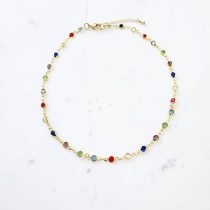 May include: A gold-toned chain necklace featuring a series of small, round, multi-colored gemstones spaced evenly along the links. The necklace includes a lobster claw clasp and an adjustable extender chain. The text "Chain 1" is visible.