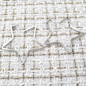 May include: A pair of silver star-shaped hoop earrings. The earrings are made of metal and have a simple, modern design.