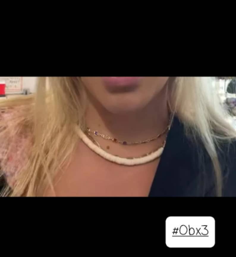 May include: A layered necklace set consisting of two distinct pieces. The top layer is a gold-toned chain featuring small, square-shaped colorful gemstones. The bottom layer is a thick, smooth, off-white beaded strand with a matte finish.