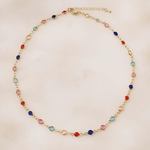 May include: A gold-tone chain necklace featuring a series of small, round, multi-colored gemstones set at regular intervals. The stones alternate in shades of red, blue, pink, and light blue, connected by thin metal links with a lobster clasp.