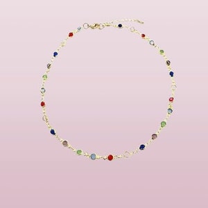 May include: A gold-toned chain necklace featuring a series of small, round, multi-colored gemstones spaced evenly along the length. The necklace includes a lobster claw clasp and an adjustable extender chain at the back for a secure fit.