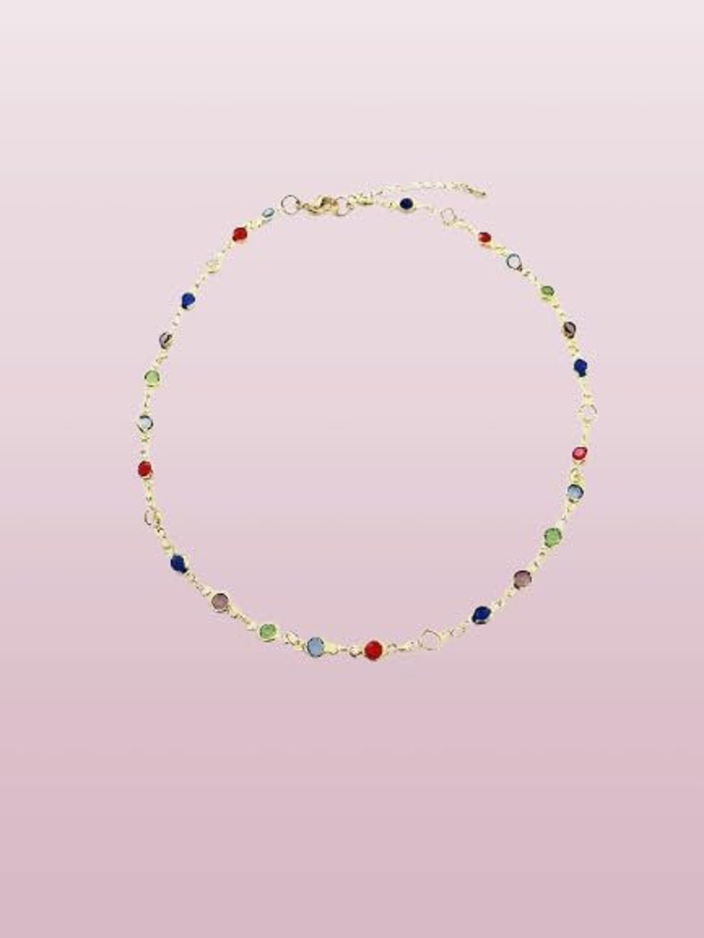 May include: A gold-toned chain necklace featuring a series of small, round, multi-colored gemstones spaced evenly along the length. The necklace includes a lobster claw clasp and an adjustable extender chain at the back for a secure fit.