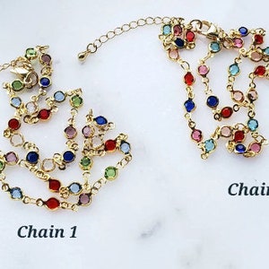 May include: Two gold-toned metal chains featuring a series of small, round, multi-colored faceted stones set in individual bezels. Each chain includes a lobster clasp and an extender link. The text Chain 1 and Chain 2 labels the items.