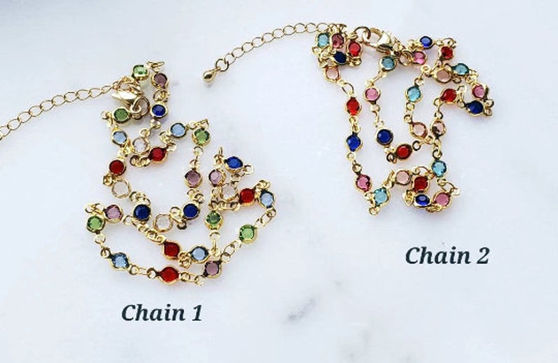 May include: Two gold-toned metal chains featuring a series of small, round, multi-colored faceted stones set in individual bezels. Each chain includes a lobster clasp and an extender link. The text Chain 1 and Chain 2 labels the items.