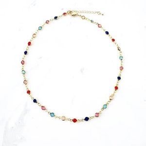 May include: A gold-tone chain necklace featuring small, round, multi-colored stones in red, blue, pink, and light blue, spaced evenly along the links. The necklace includes a lobster claw clasp and an adjustable extender chain. Text reads Chain 2.