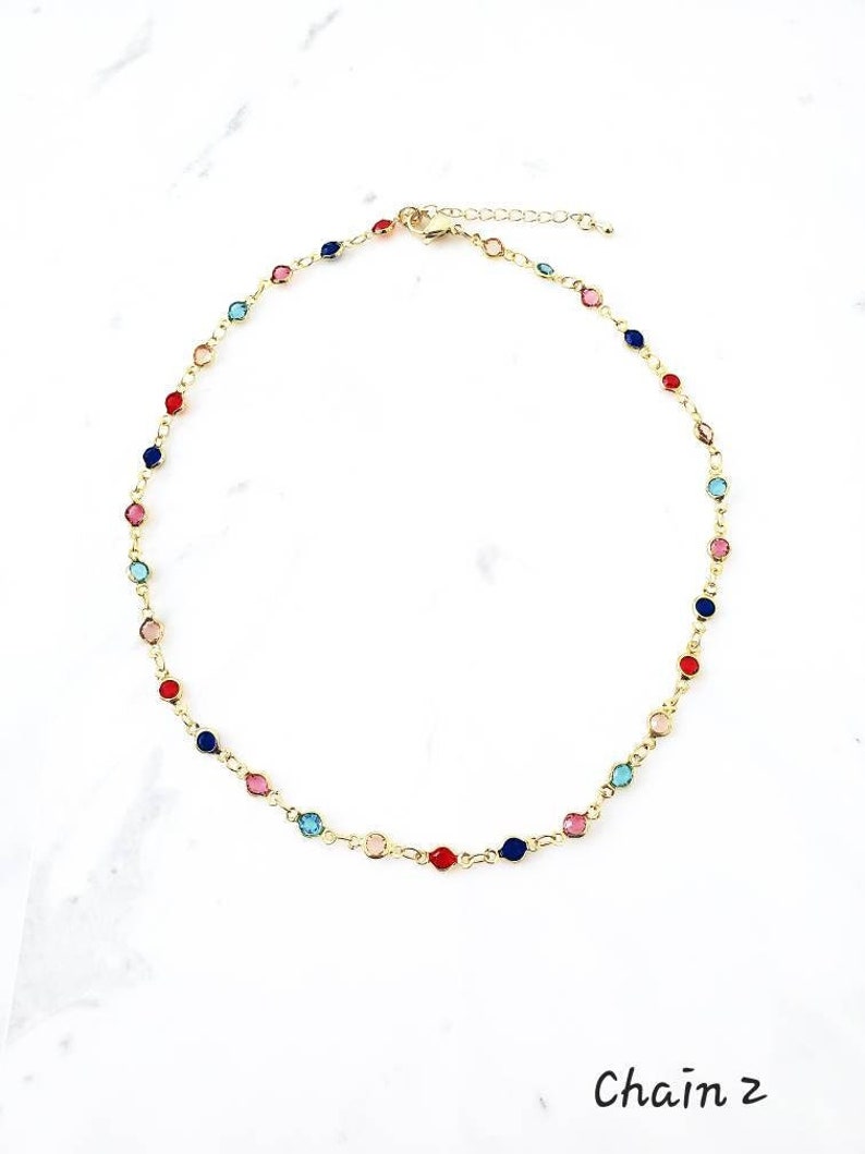 May include: A gold-tone chain necklace featuring small, round, multi-colored stones in red, blue, pink, and light blue, spaced evenly along the links. The necklace includes a lobster claw clasp and an adjustable extender chain. Text reads Chain 2.