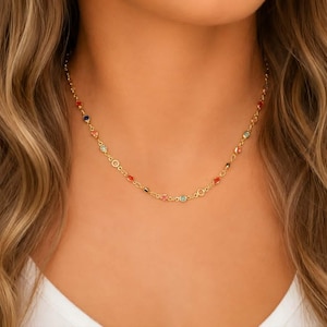 May include: A gold chain necklace featuring small, evenly spaced, multi-colored gemstones in shades of red, blue, and light green. The delicate metal links connect each stone, creating a continuous, lightweight design that rests around the neck.