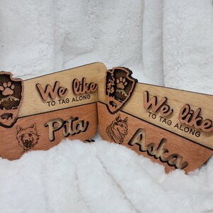 May include: Two wooden signs with the text "We like to tag along" and the names "Pita" and "Aska". Each sign features a wood-burned image of a dog and a national park emblem.