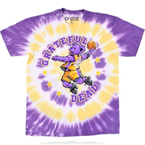 May include: Purple, yellow, and white tie-dye t-shirt featuring a cartoon bear wearing a basketball uniform and holding a basketball. The bear is surrounded by stars and the words "Grateful Dead" are written in a circle around the bear.