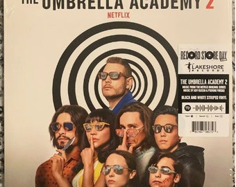 May include: A black and white vinyl record with a target design and the text "The Umbrella Academy 2" in white. The record is from the Netflix original series and features music by Jeff Russo & Perrine Virgili. The record is on a black background with a white border.