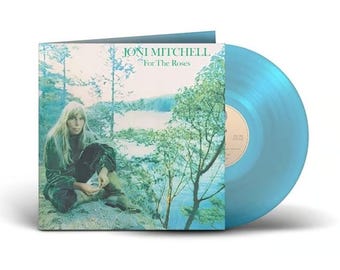 May include: A vinyl record album titled "For The Roses" by Joni Mitchell. The album cover features a woman sitting near a lake. The record itself is a light blue color.