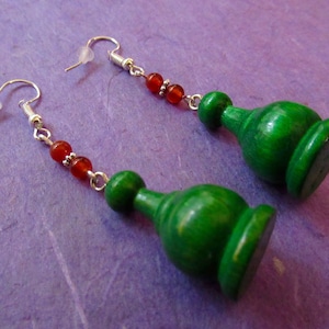 Może przedstawiać: Para zielonych drewnianych kolczyków z czerwonymi koralikami z kamieni szlachetnych i srebrnymi haczykami.