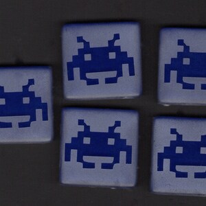 May include: Five blue ceramic tiles with a white outline of a space invader graphic on each tile.
