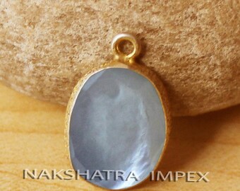 Può includere: Un ciondolo dorato con una pietra ovale blu chiaro. Il ciondolo ha un piccolo anello nella parte superiore per una catena. Il testo "NAKSHATRA IMPEX" è stampato nella parte inferiore del ciondolo. Il ciondolo è posto su uno sfondo strutturato.