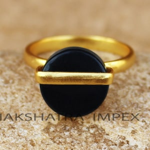 May include: A gold ring with a black round stone and a gold band across the center.