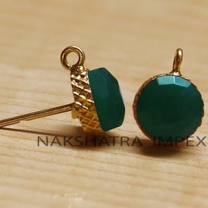 Puede incluir: Dos hallazgos de pendientes de tono dorado con acentos de piedras preciosas verdes. Los hallazgos tienen un bucle en la parte superior y un poste en la parte inferior. Las piedras preciosas son redondas y tienen un acabado facetado.