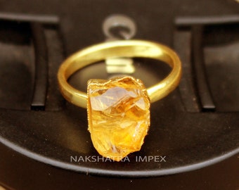 May include: A gold ring with a large, rough-cut, yellow citrine gemstone. The ring is set on a black background.