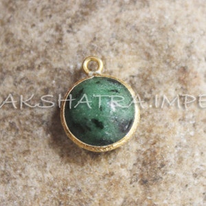 May include: A gold pendant with a green gemstone. The gemstone has a dark green color with black flecks.