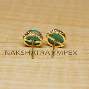 May include: A pair of gold stud earrings with green gemstone accents. The earrings have a simple design and are perfect for everyday wear.