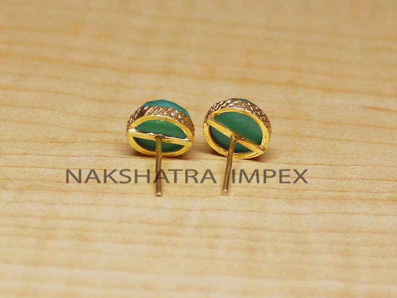 May include: A pair of gold stud earrings with green gemstone accents. The earrings have a simple design and are perfect for everyday wear.