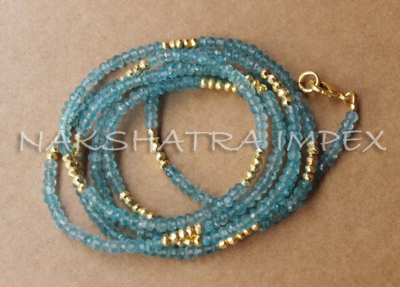 Puede incluir: Un collar de m&uacute;ltiples hilos hecho de cuentas de color azul claro y dorado. El collar est&aacute; hecho de m&uacute;ltiples hilos de cuentas peque&ntilde;as y redondas, algunas de las cuales son doradas y otras de color azul claro. El collar est&aacute; unido por un cierre dorado.