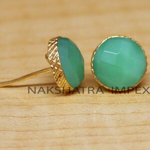 May include: A pair of gold earrings with green gemstone cabochons. The earrings have a textured gold setting.