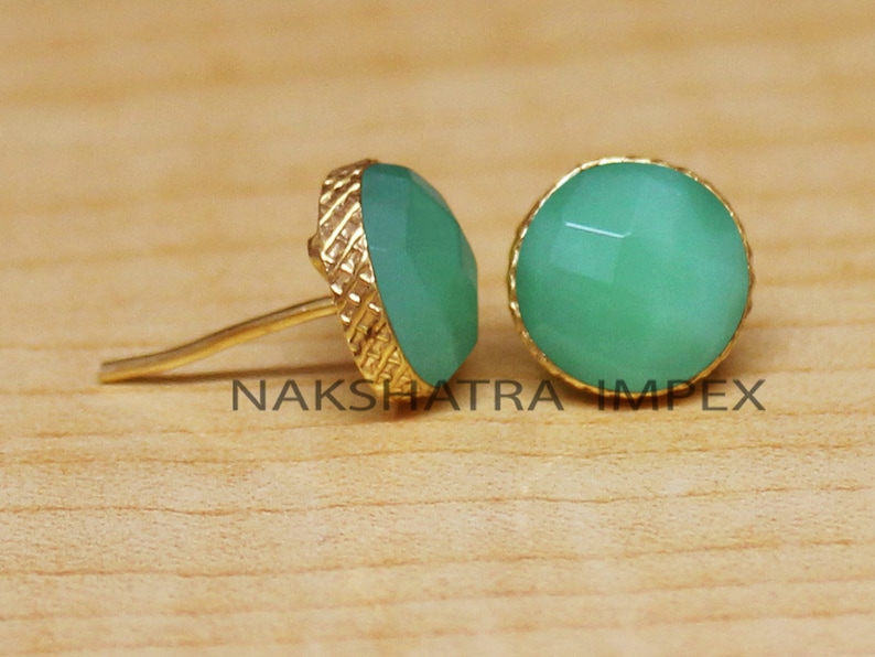 May include: A pair of gold earrings with green gemstone cabochons. The earrings have a textured gold setting.