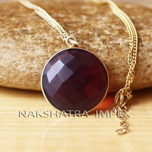 Puede incluir: Un collar de cadena de oro con un colgante redondo con una piedra preciosa de color púrpura oscuro.