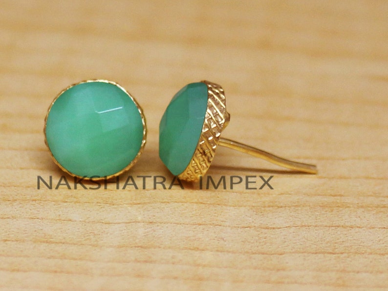 May include: A pair of gold stud earrings with green gemstone accents. The gemstones are faceted and have a rounded shape.