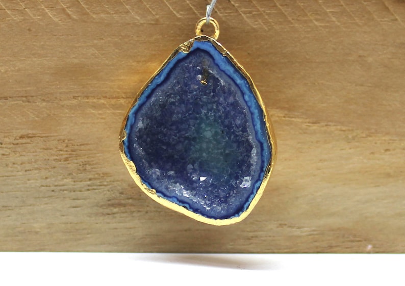 May include: A gold-plated pendant featuring a blue agate geode with a natural crystal formation. The pendant has a smooth, polished surface and a gold-colored rim.
