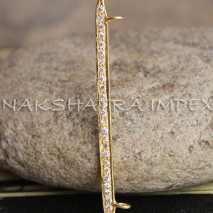 May include: Gold-toned pendant with a pointed tip and two loops. The pendant is adorned with a row of clear cubic zirconia stones.