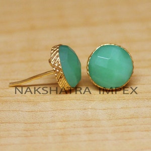 May include: A pair of gold stud earrings with green gemstone accents. The earrings have a textured gold setting.