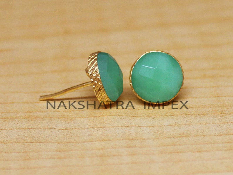 May include: A pair of gold stud earrings with green gemstone accents. The earrings have a textured gold setting.