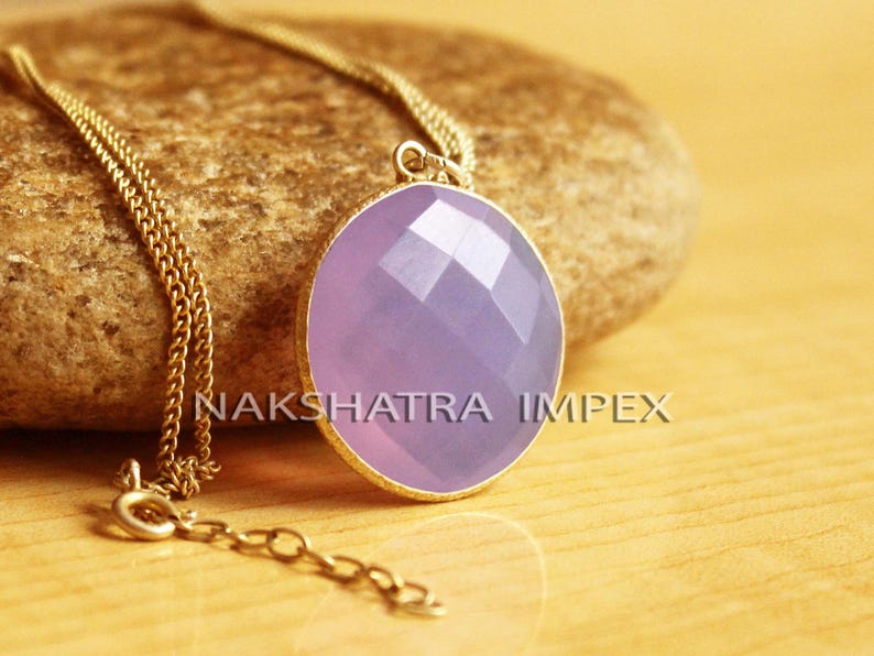 May include: A gold chain necklace with a lavender oval pendant. The pendant has a faceted design.